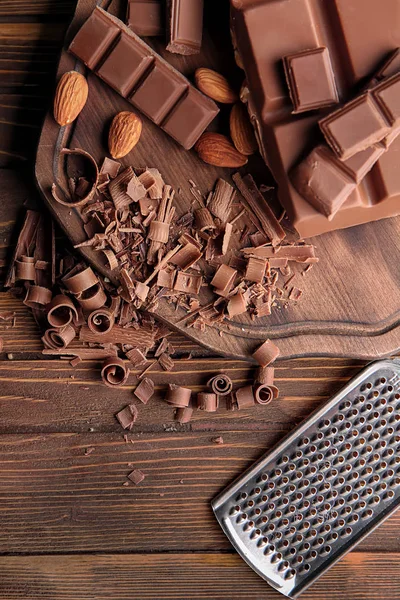 Schokoladenstücke mit Mandeln und Reibe auf Holztisch — Stockfoto