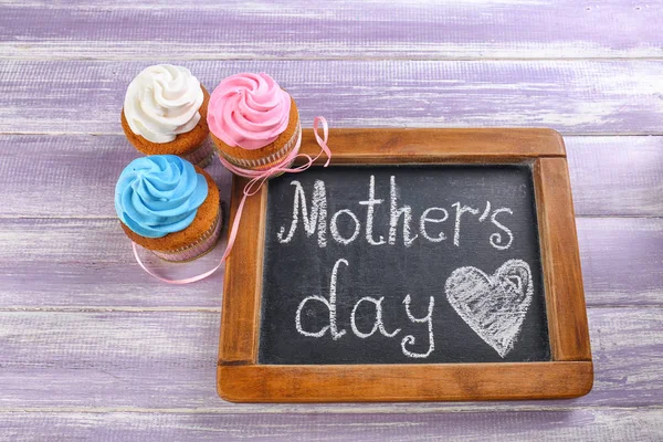 Cupcakes saborosos e quadro-negro com palavras MÃE 'S DAY na mesa de madeira — Fotografia de Stock