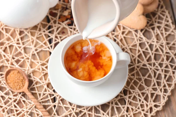 Pouring milk into cup with aromatic tea on wicker mat — Stock Photo, Image