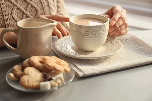 Жінка тримає чашку ароматного чаю з молоком за столом — стокове фото