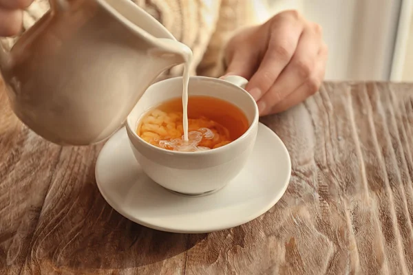 Woman pouring milk into cup with aromatic tea on table — Stock Photo, Image