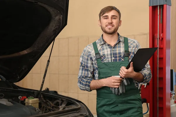 Joven mecánico de automóviles con portapapeles cerca de coche en el centro de servicio — Foto de Stock