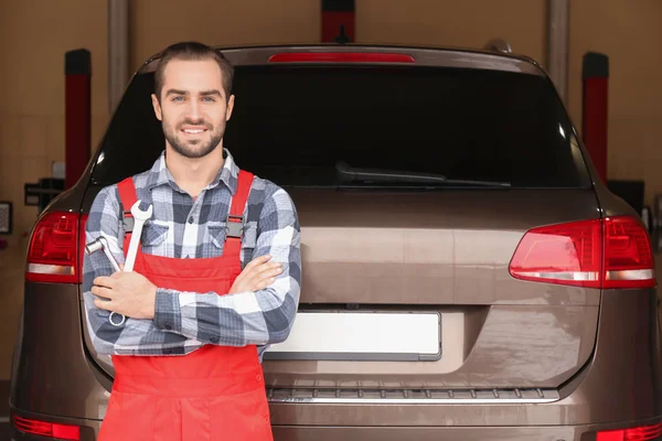 Young auto mechanic with tools near car in service center — Stock Photo, Image