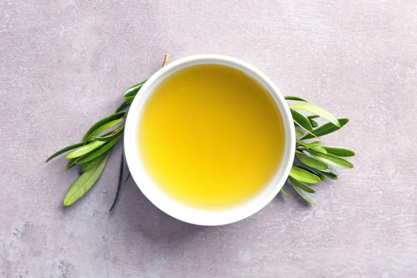 Cuenco con aceite de oliva y hojas verdes sobre fondo gris, vista superior — Foto de Stock