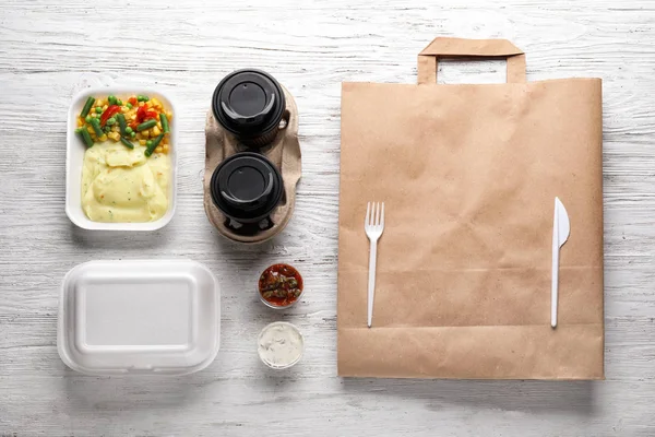 Plastic bakjes met heerlijke gerechten, kartonnen bekers en tas op houten tafel. Leveringsservice — Stockfoto