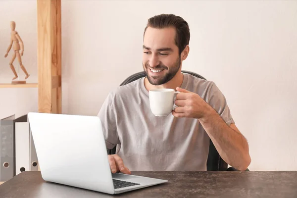 Male freelancer drinking tea while working with laptop in home office — Stock Photo, Image