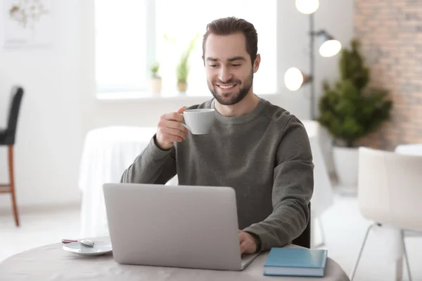 Αρσενικό freelancer πίνοντας καφέ ενώ εργάζεστε με το φορητό υπολογιστή στο γραφείο στο σπίτι — Φωτογραφία Αρχείου