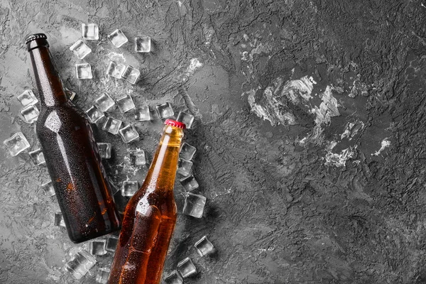 Свіже пиво в скляних пляшках і кубиках льоду на сірому фоні — стокове фото