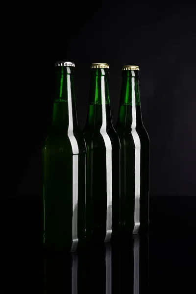 Cerveja fresca em garrafas de vidro sobre fundo preto — Fotografia de Stock