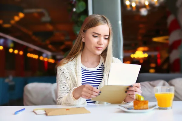 Jovem mulher lendo carta à mesa no café. Entrega de correio — Fotografia de Stock