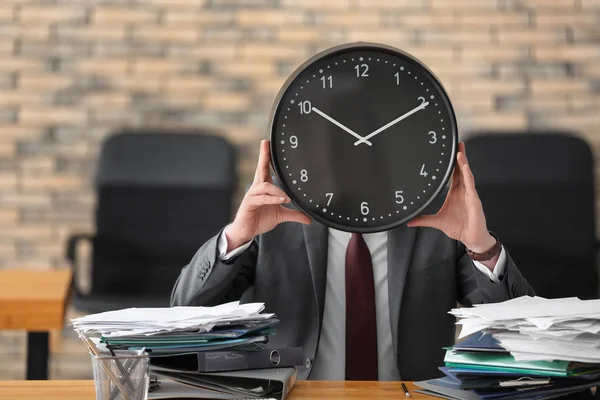 Hombre escondiendo la cara detrás del reloj en la mesa en la oficina. Concepto de gestión del tiempo — Foto de Stock