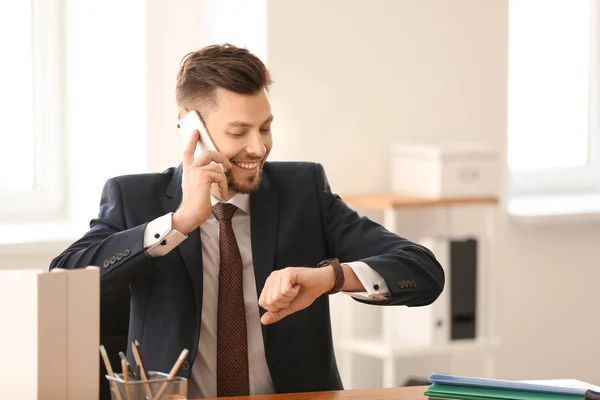 Бизнесмен с мобильным телефоном смотрит на наручные часы в офисе. Концепция управления временем — стоковое фото