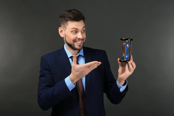 Businessman with hourglass on dark background. Time management concept