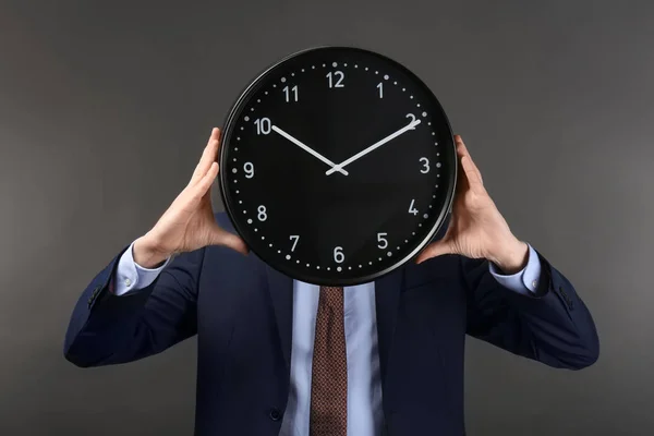 Man hiding face behind clock on dark background. Time management concept