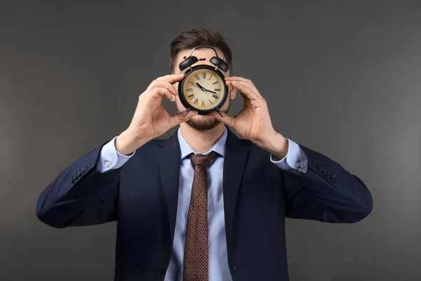 Hombre escondiendo la cara detrás del despertador sobre fondo oscuro. Concepto de gestión del tiempo — Foto de Stock