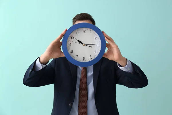 Homem escondendo o rosto atrás do relógio no fundo da cor. Conceito de gestão do tempo — Fotografia de Stock