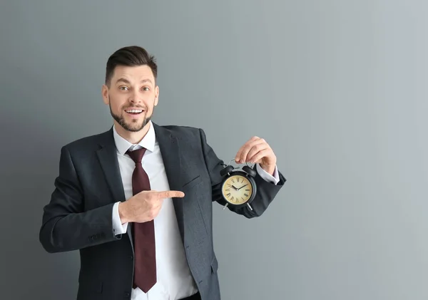 Empresário com despertador no fundo cinza. Conceito de gestão do tempo — Fotografia de Stock