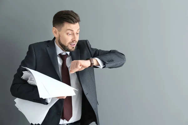 Geschäftsmann mit Papieren, die auf seine Armbanduhr vor grauem Hintergrund schauen. Zeitmanagement-Konzept — Stockfoto