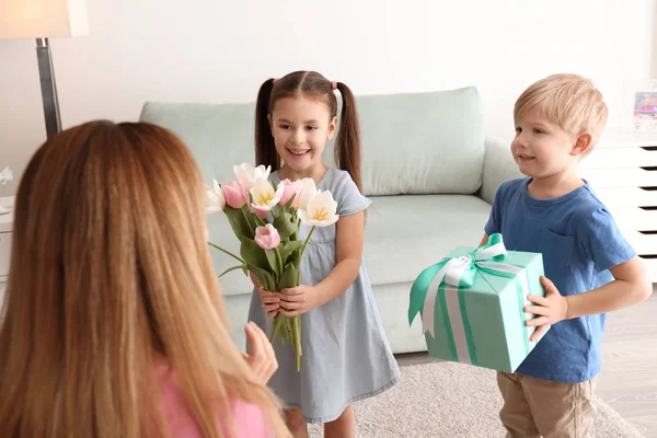 Mother receiving gift and flowers from her cute little children at home — Stock Photo, Image