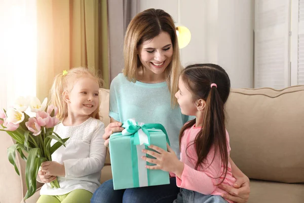 Mother receiving gift and flowers from her cute little daughters at home — Stock Photo, Image