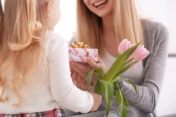 Mother receiving gift and flowers from her cute little daughter at home