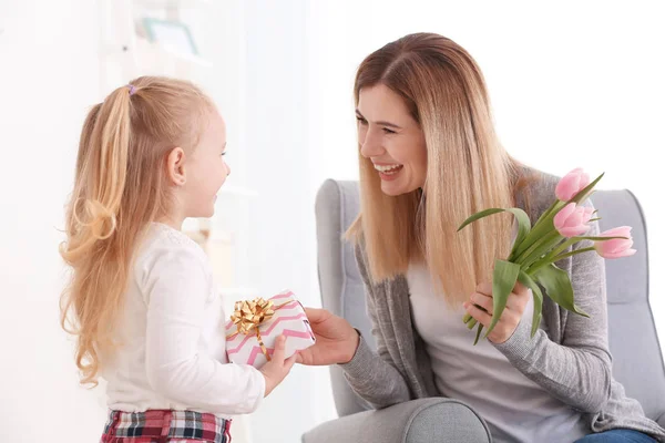 Mother receiving gift and flowers from her cute little daughter at home — Stock Photo, Image