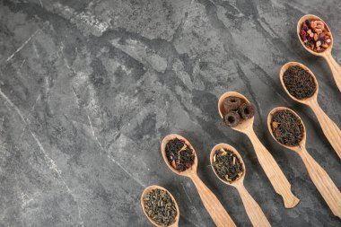 Düz gri dokulu arka plan üzerinde kaşık çay farklı türde, lay
