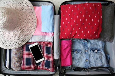 Giysi, hasır şapka ve cep telefonu açık bavul, üstten görünüm katlanmış