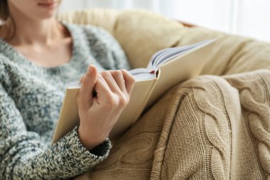 Genç kadın, evde koltuk içinde kitap okumak