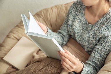Genç kadın, evde koltuk içinde kitap okumak