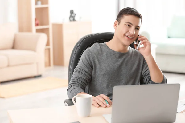 Молодий чоловік розмовляє по телефону під час роботи з ноутбуком в домашньому офісі — стокове фото