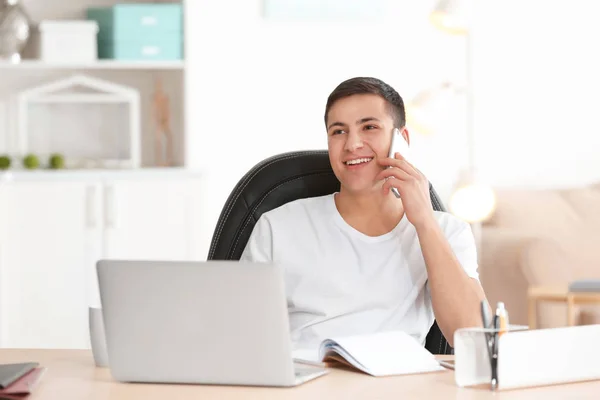 Νεαρός άνδρας μιλάει στο τηλέφωνο ενώ εργάζεστε με το φορητό υπολογιστή στο γραφείο στο σπίτι — Φωτογραφία Αρχείου