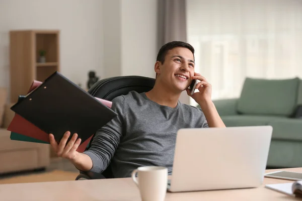 Jeune homme parlant au téléphone tout en travaillant avec ordinateur portable dans le bureau à la maison — Photo