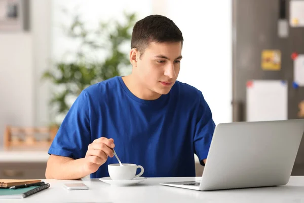 Jovem bebendo café enquanto trabalhava com laptop no escritório em casa — Fotografia de Stock