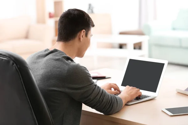 Ung man arbetar med laptop vid bord i hemmakontoret — Stockfoto