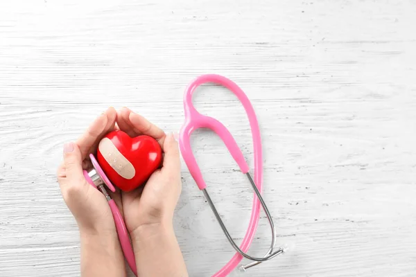 Frau mit rotem Herz mit medizinischem Pflaster auf hölzernem Hintergrund. Gesundheitskonzept — Stockfoto