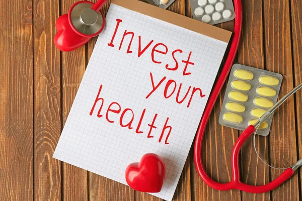 "あなたの健康"、紙、聴診器や木製の背景に薬に書かれてと投資をフレーズします。 — ストック写真