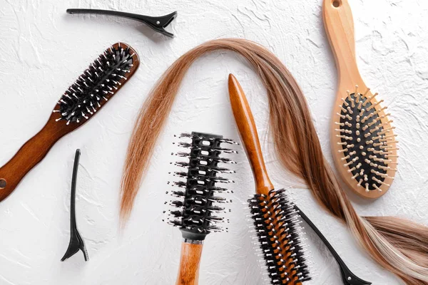 Diferentes cepillos y hebra de cabello sobre fondo texturizado blanco — Foto de Stock