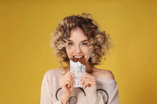 Portret van mooie jonge vrouw die het eten van chocolade op kleur achtergrond — Stockfoto