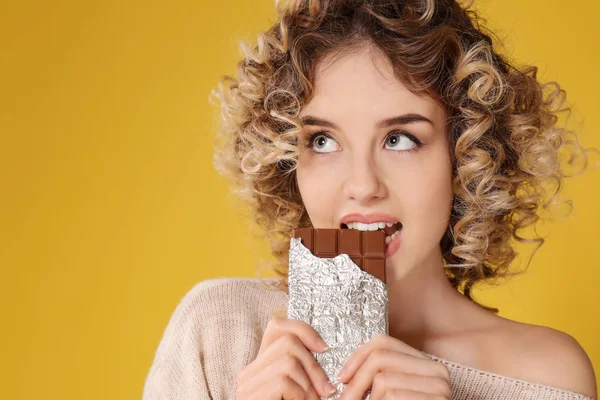 Porträt der schönen jungen Frau, die Schokolade auf farbigem Hintergrund isst — Stockfoto
