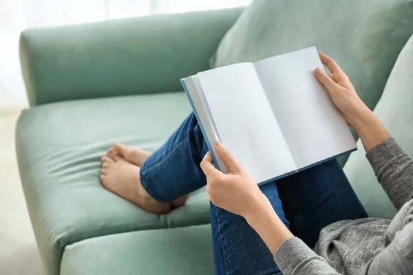 Young woman reading book on sofa at home — Stock Photo, Image