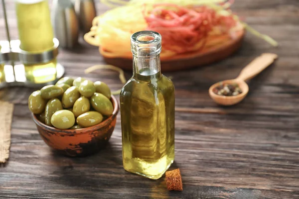 Bottle with oil and olives on wooden table — Stock Photo, Image