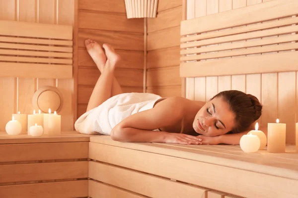 Mujer joven acostada en un banco de madera en la sauna — Foto de Stock