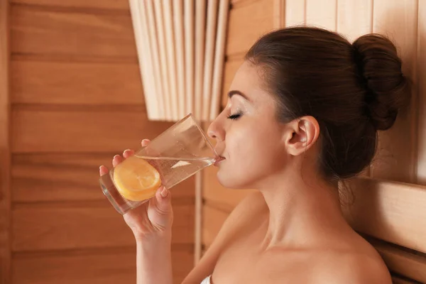 年轻美丽的妇女喝冷水与柠檬在桑拿浴 — 图库照片