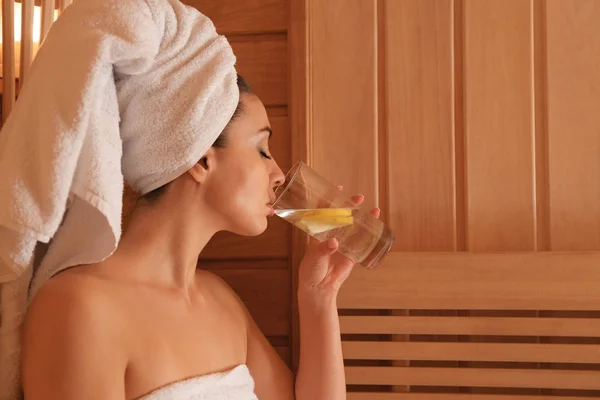 Joven hermosa mujer bebiendo agua fría con limón en la sauna — Foto de Stock