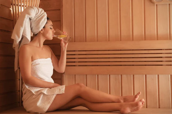 年轻美丽的妇女喝冷水与柠檬在桑拿浴 — 图库照片