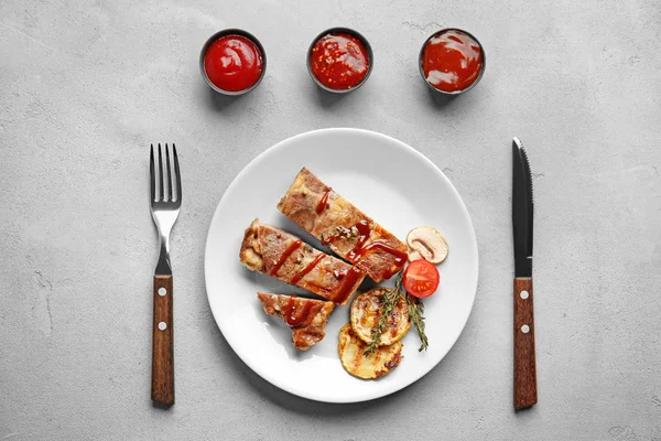 Plate of grilled meat with vegetables and barbecue sauces in bowls on table, top view