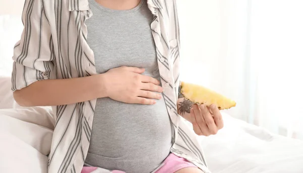 Hermosa mujer embarazada con rebanada de piña en la cama por la mañana — Foto de Stock