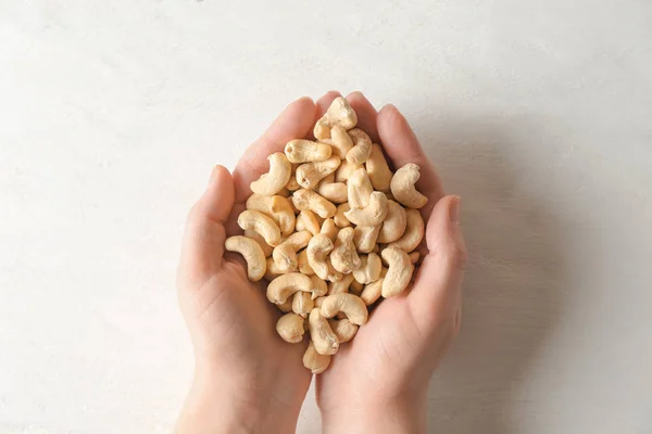 Female hands with tasty cashew nuts on light background — Stock Photo, Image