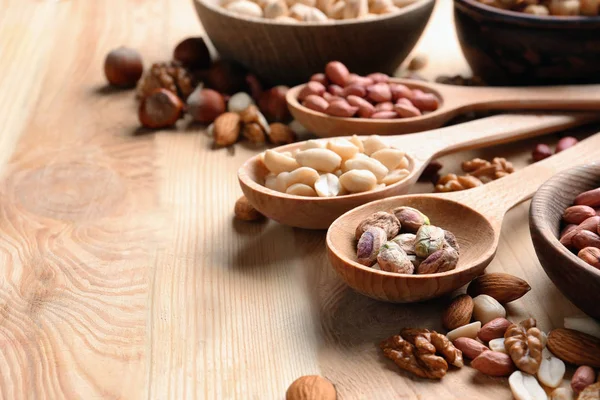 Cucharas con diferentes nueces en mesa de madera — Foto de Stock